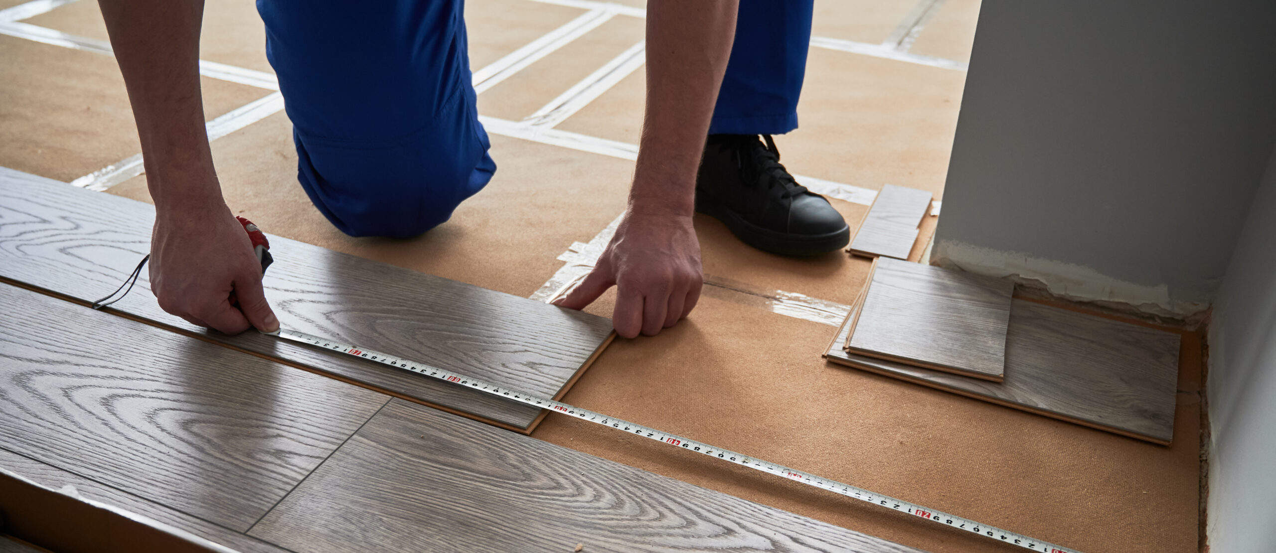 Männliche Hände messen den Abstand von der Wand zur Laminatbodendiele.